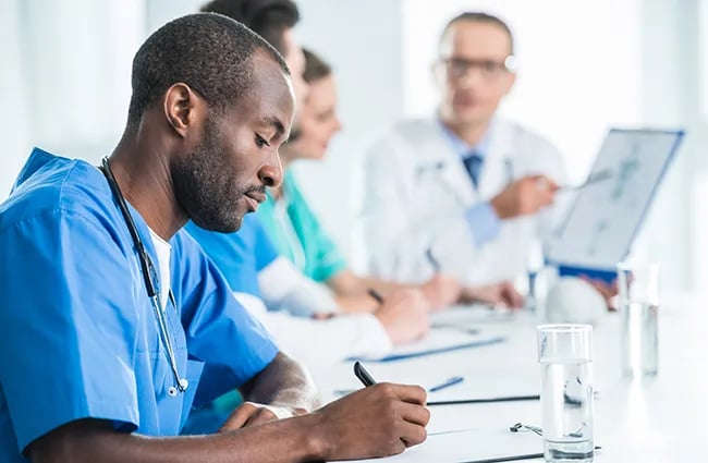 Healthcare professional writing on clipboard at a conference table