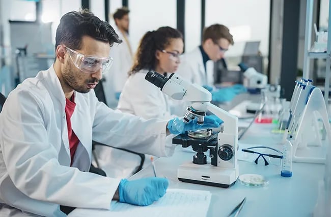 Row of lab techs wearing protective equipment working on various medical devices