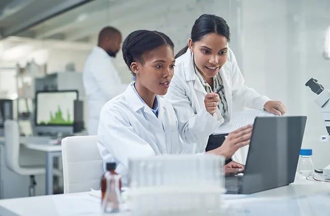 Two women in lab coats reviewing a laptop in a laboratory