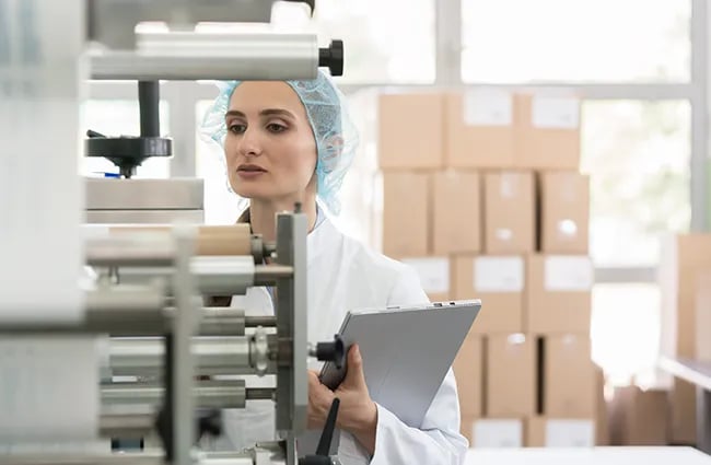 Woman in hairnet holding laptop investigating machines