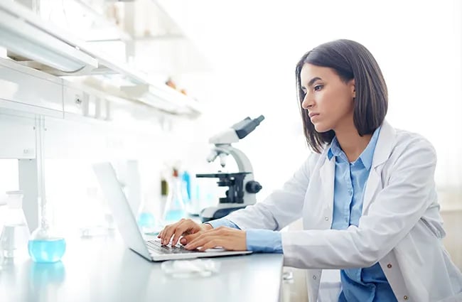 Woman in lab coat typing on laptop in a lab
