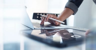 Hand holding pen between fingers typing on laptop and using tablet device