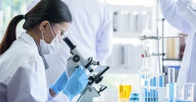 Woman wearing protective equipment looking into microscope