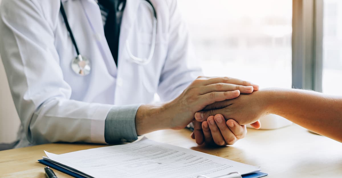 Doctor holding a patient's hand over a desk