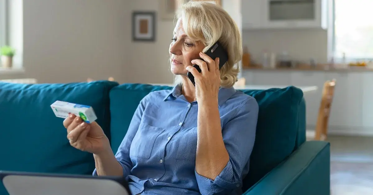 Elderly woman checking medication information while on the phone.