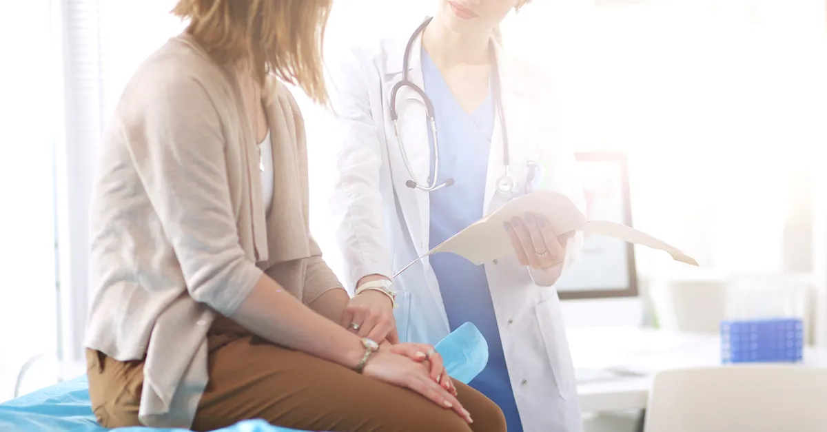 Patient sitting on examination table talking to healthcare professional holding an open folder