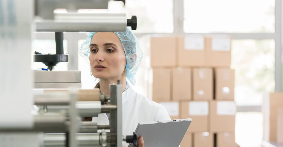 Woman in hairnet holding laptop investigating machines